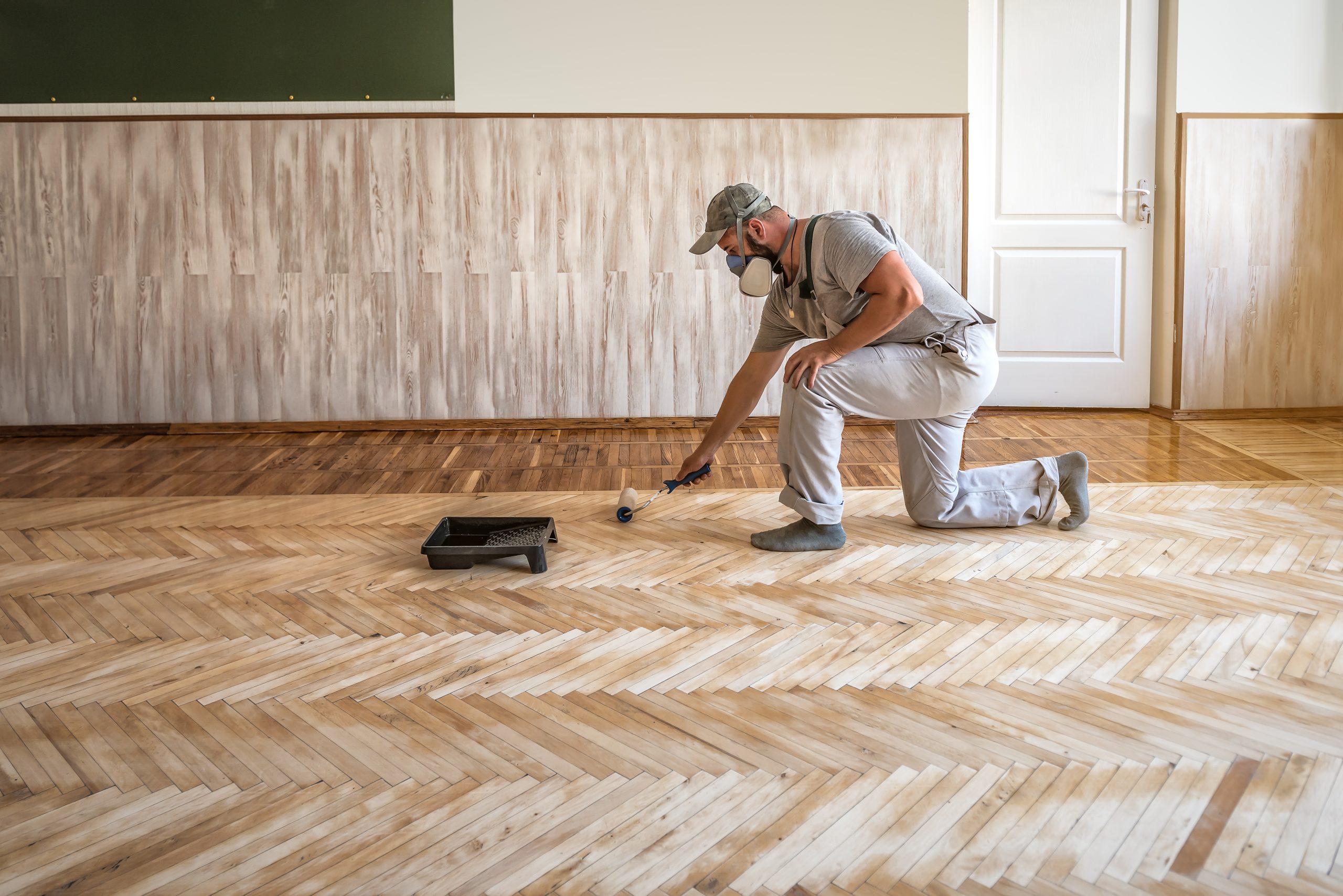 Worker rolling on a clear sealant while Restoring Classic Herringbone oak parquet flooring in a Rainham property.
