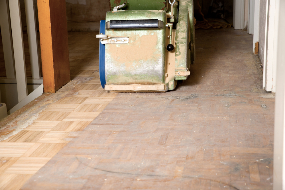 Wood Floor Sanding in Rainham on an oak mosaic parquet hallway floor, showing a sanding machine revealing fresh, clean timber.